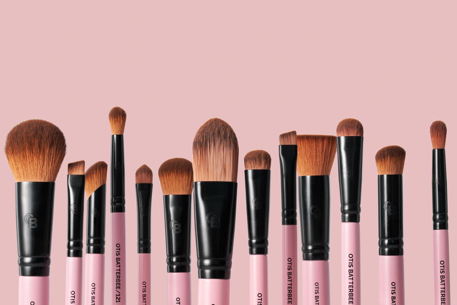 Makeup brushes with pink handles and black ferrules on a pink background