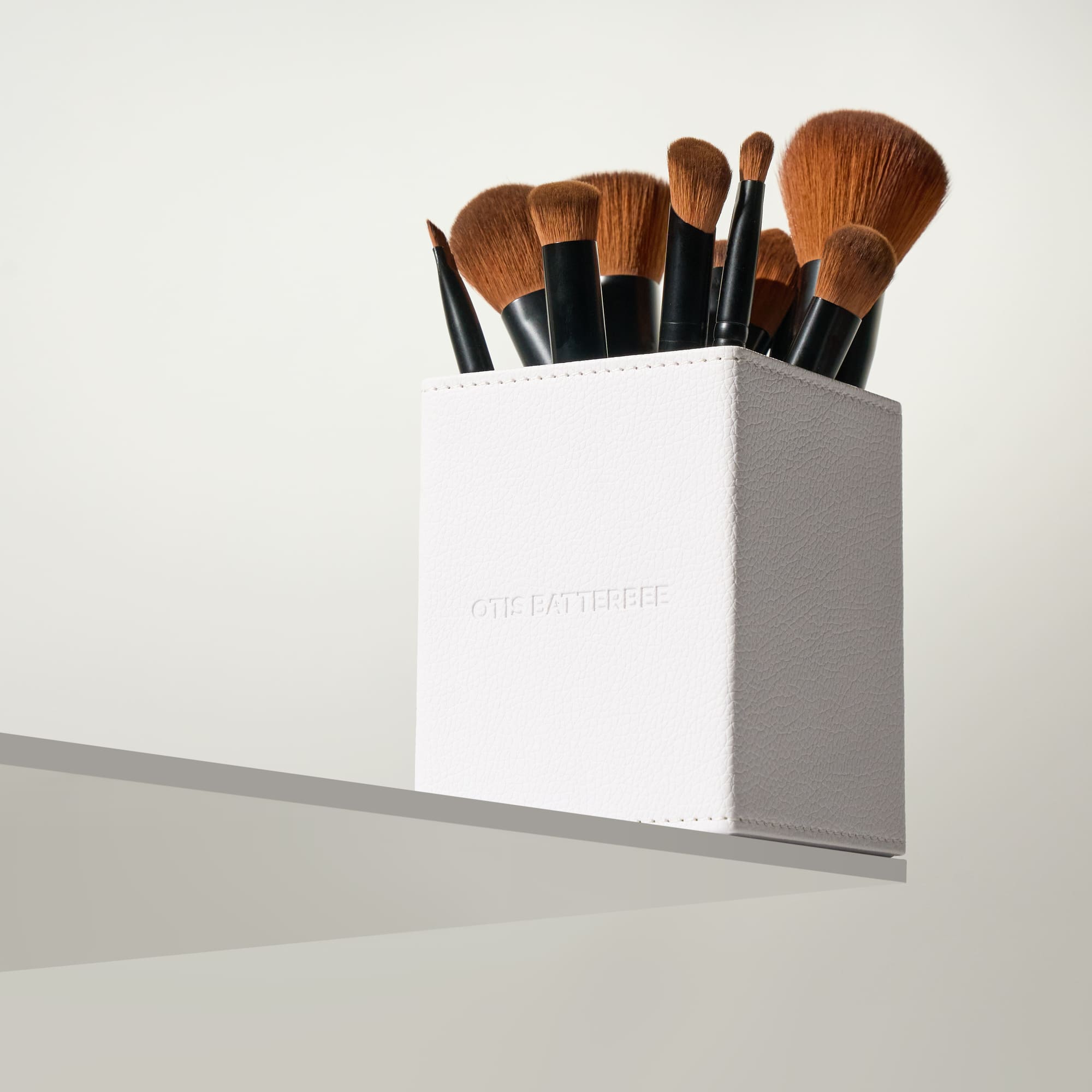 Set of makeup brushes in a white holder on a light gray background